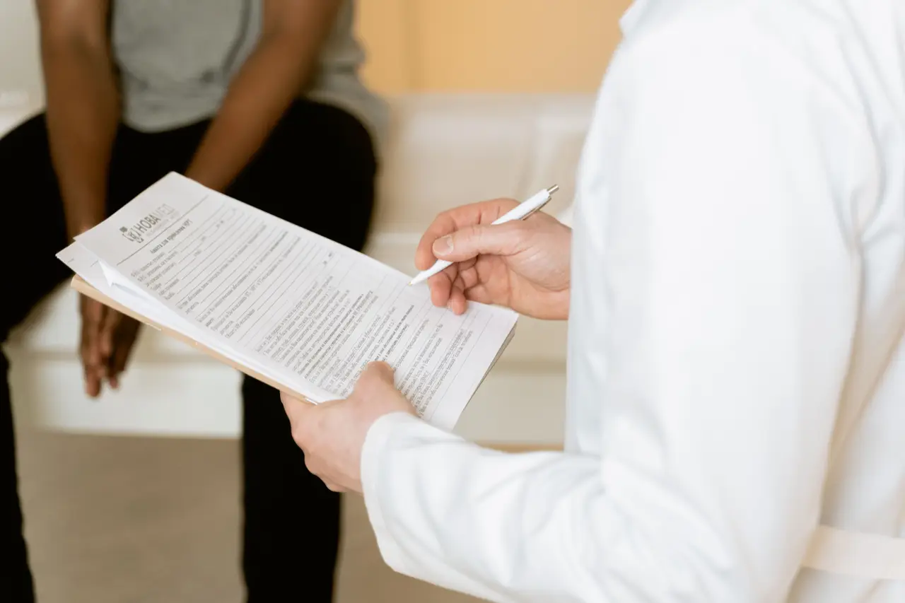 Stock photo: a clinician holding a printed form while a person waits, faces not shown